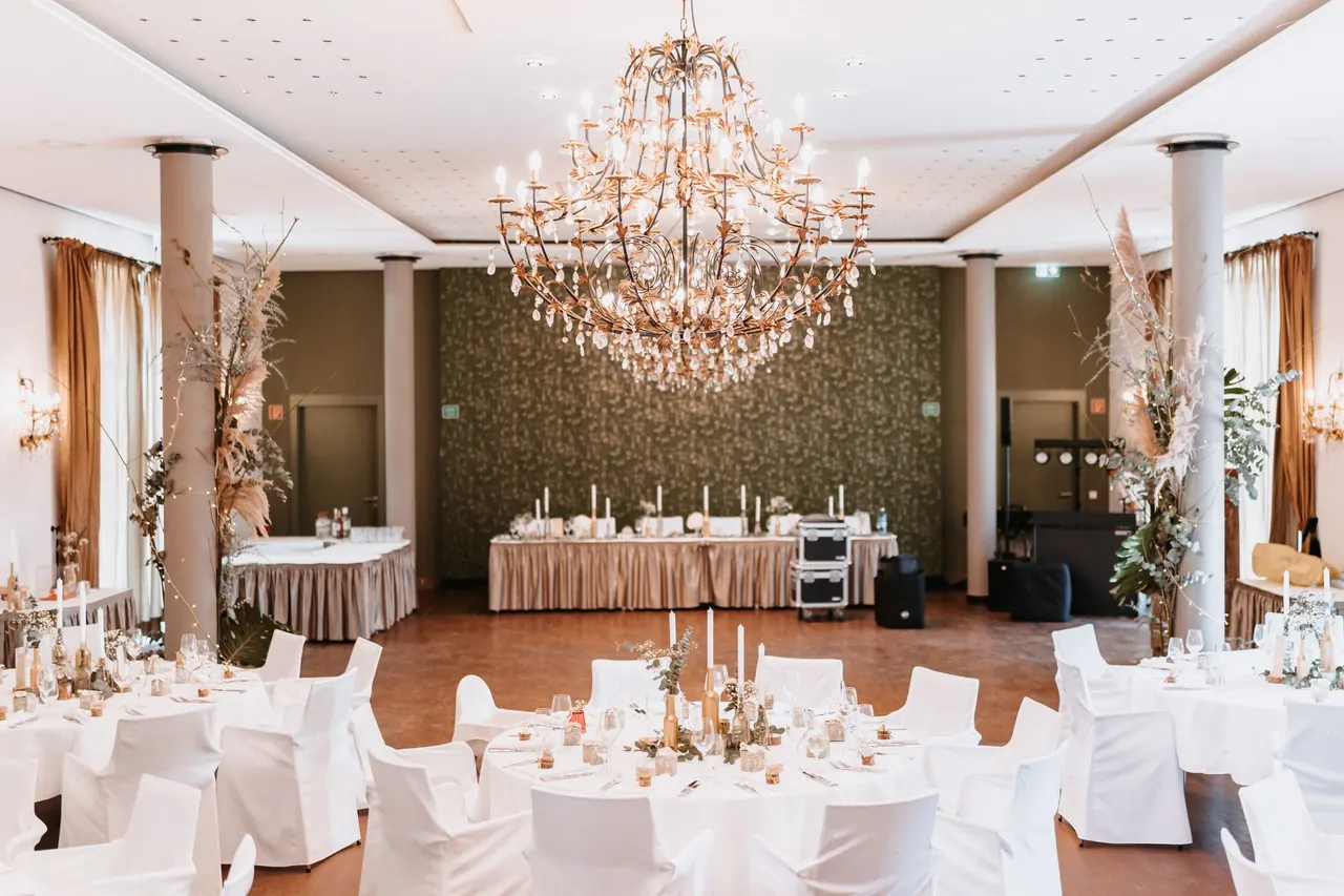 Salón de banquete con lámpara de araña y mesas vestidas de blanco